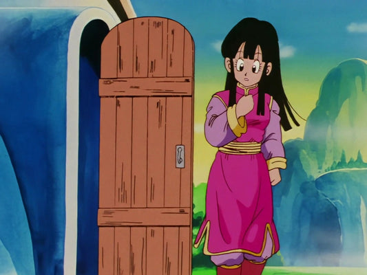 Chichi en robe rose à manches mauves, debout près de la porte en bois d'une maison arrondie, devant des montagnes verdoyantes