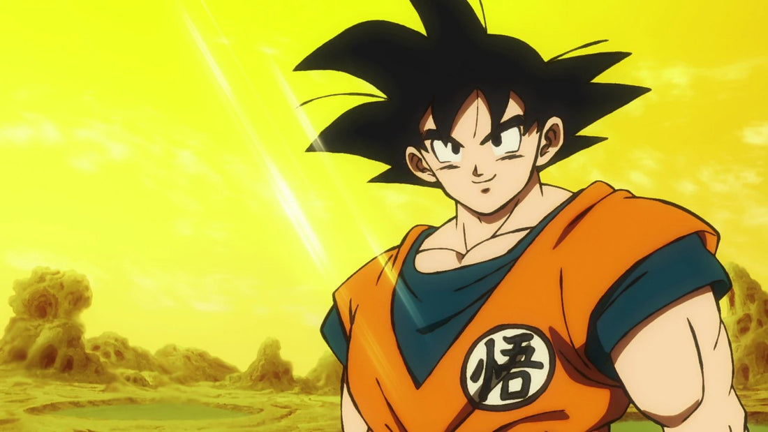 Goku adulte souriant, cheveux noirs en pointes, en tenue orange et bleue marquée d'un kanji, sous un ciel jaune au-dessus d'un sol rocheux.