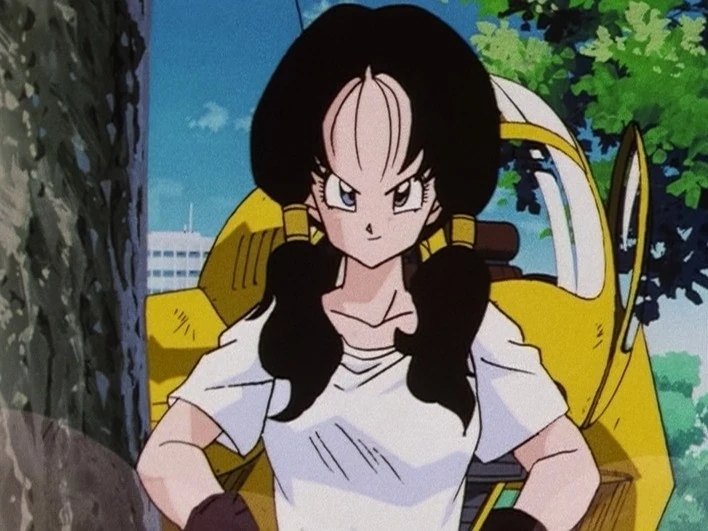Videl, couettes noires et t-shirt blanc, poings sur les hanches et sourire en coin devant son appareil volant jaune, sous les arbres.